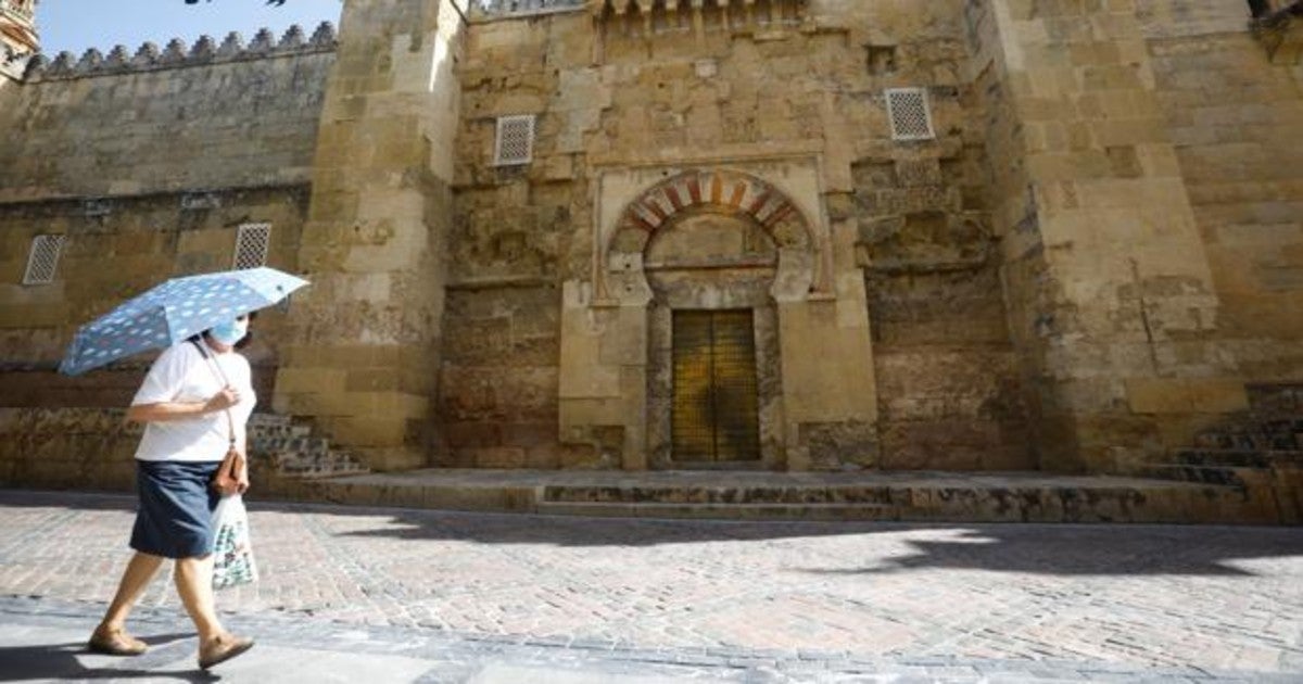 Una señora camina delante de la Mezquita-Catedrla de Córdoba bajo un paraguas