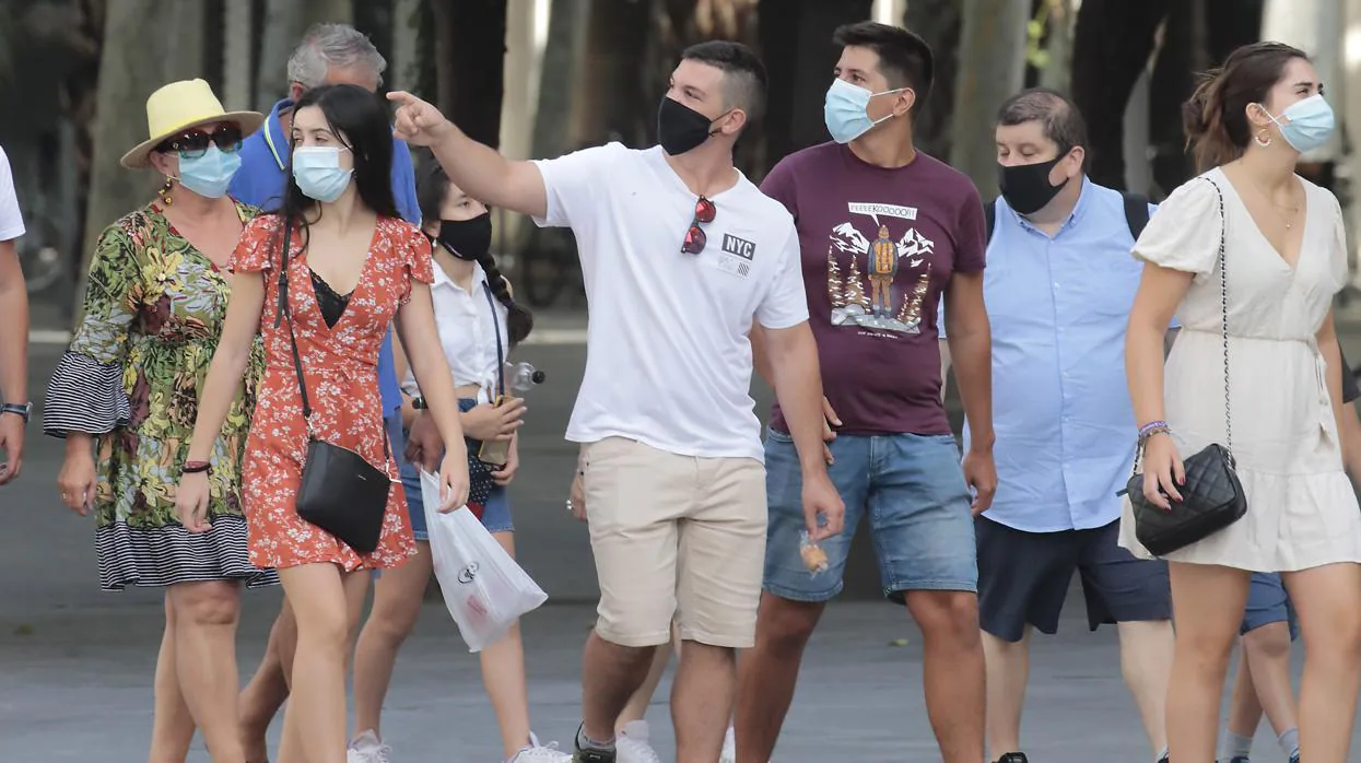 Unos jóvenes pasean con mascarilla por el centro de Sevilla