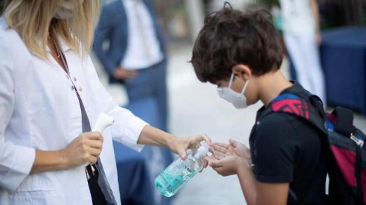 Un niño se desinfecta las manos después de que le tomen la temperatura a la entrada del colegio