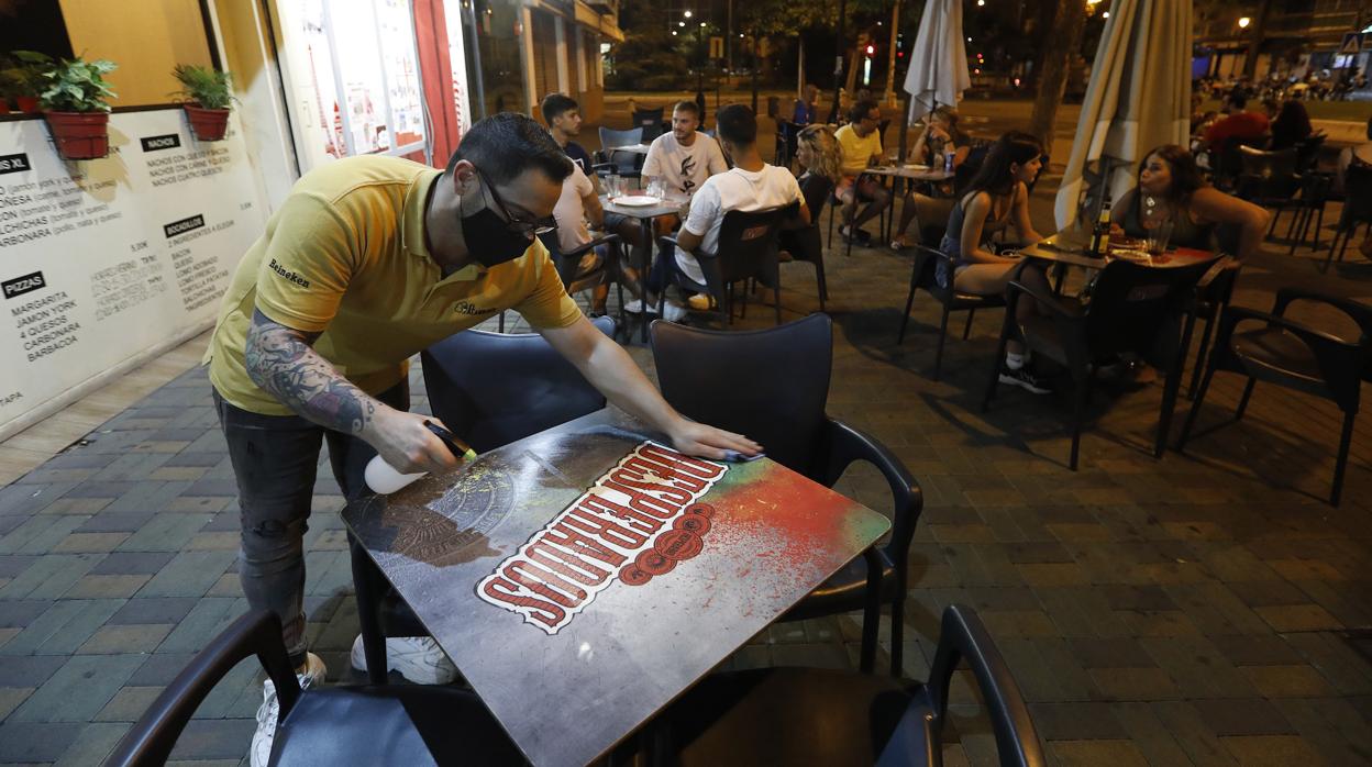 Un trabajador de un bar limpia una mesa en la avenida de Barcelona