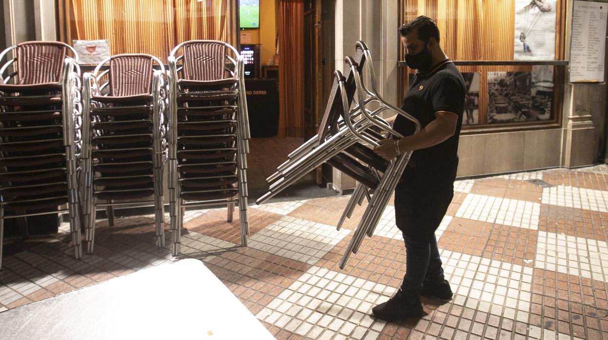 Un camarero recoge los veladores de un bar en la calle de la Plata antes de las diez de la noche