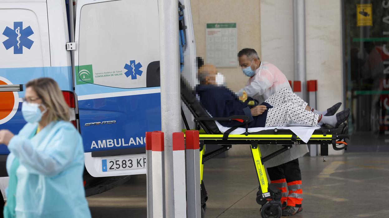 Un santiario acompaña a un paciente en camilla en la puerta de Urgencias del Reina Sofía