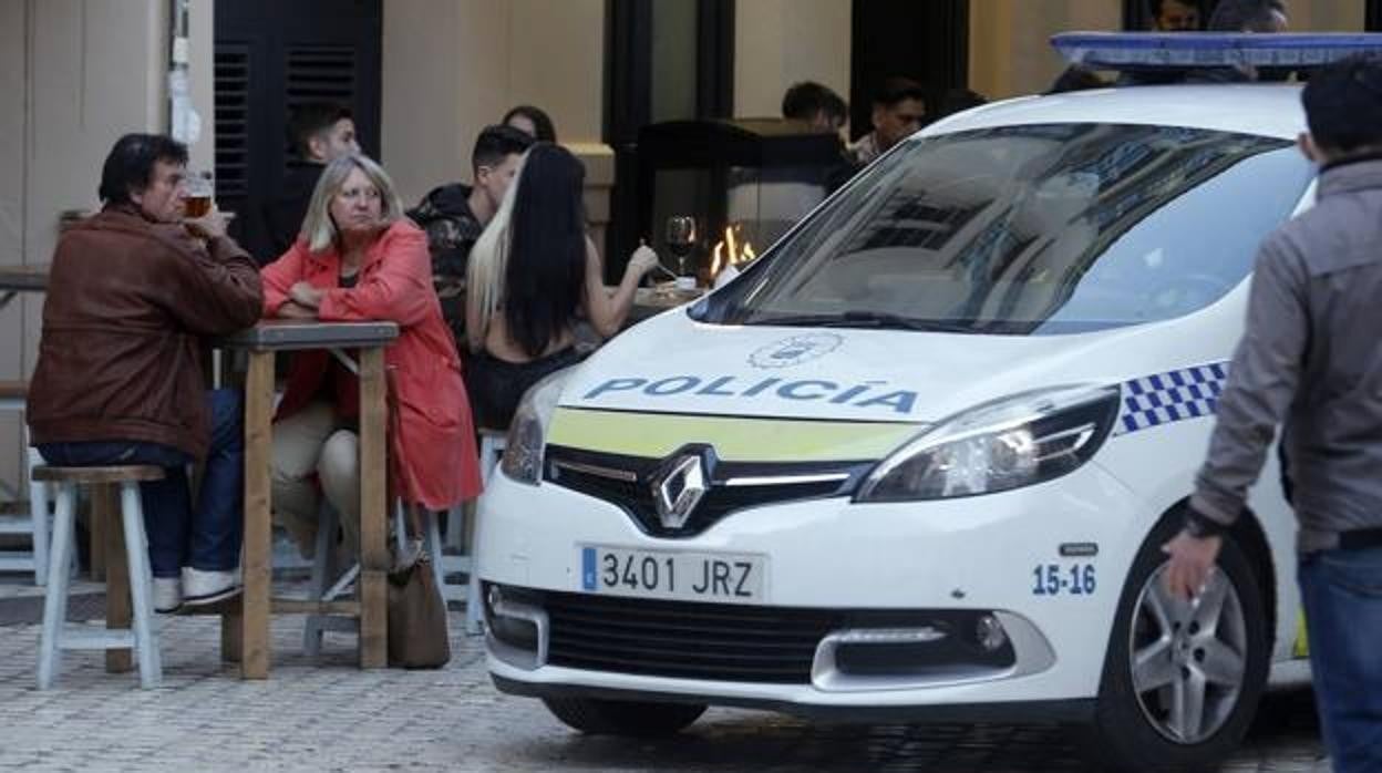 Una patrulla de la Policía Local pasa junto a una terraza en el centro de Málaga