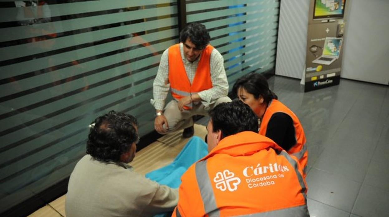 Voluntarios de Cáritas atienden a una persona sin hogar en un cajero automático