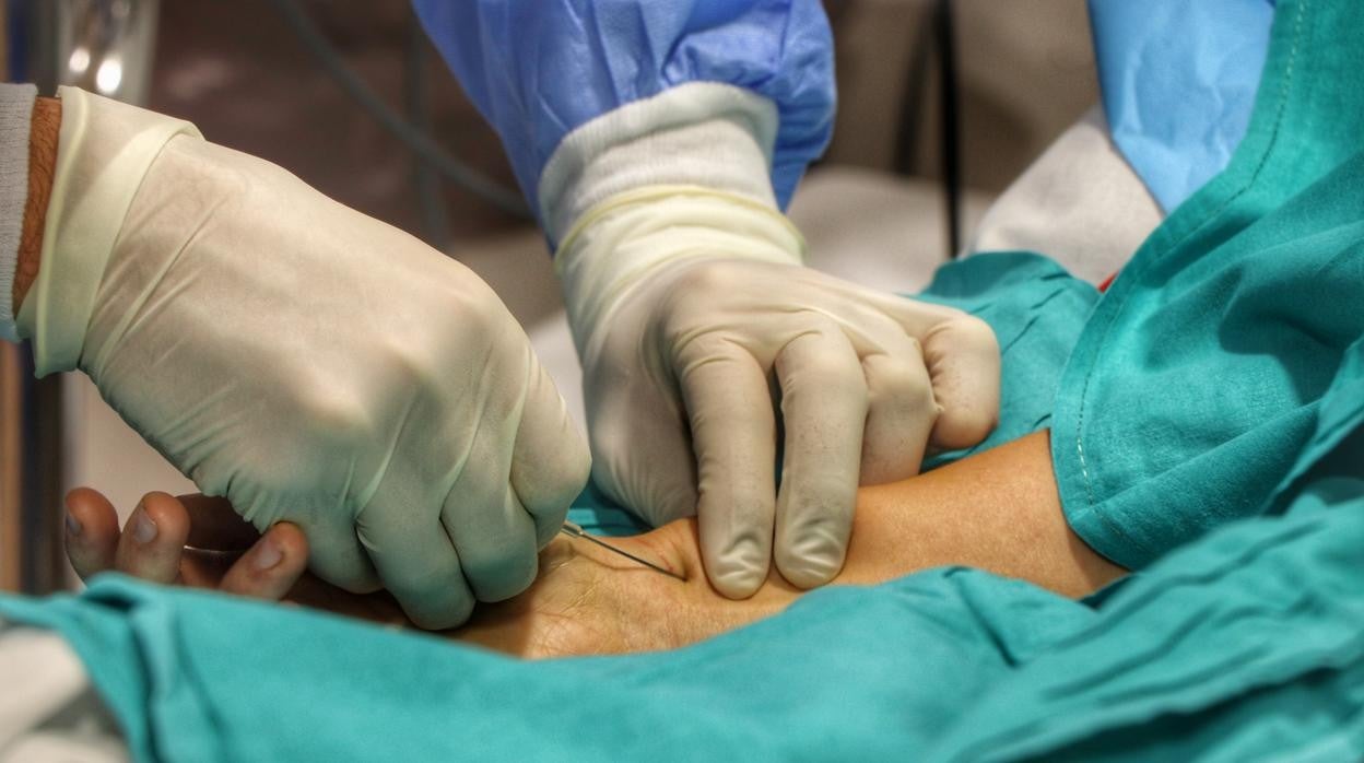 Un sanitario del Reina Sofía toma una vía a un paciente de la UCI