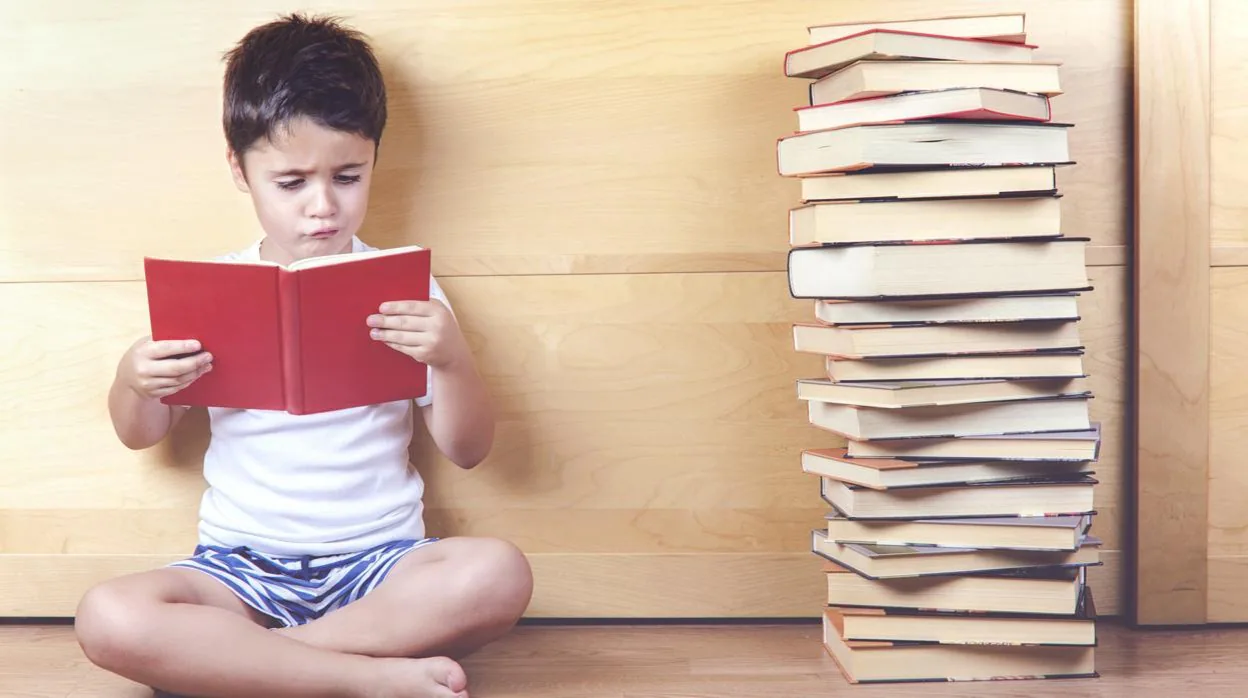 Un niño lee con una pila de libros al lado