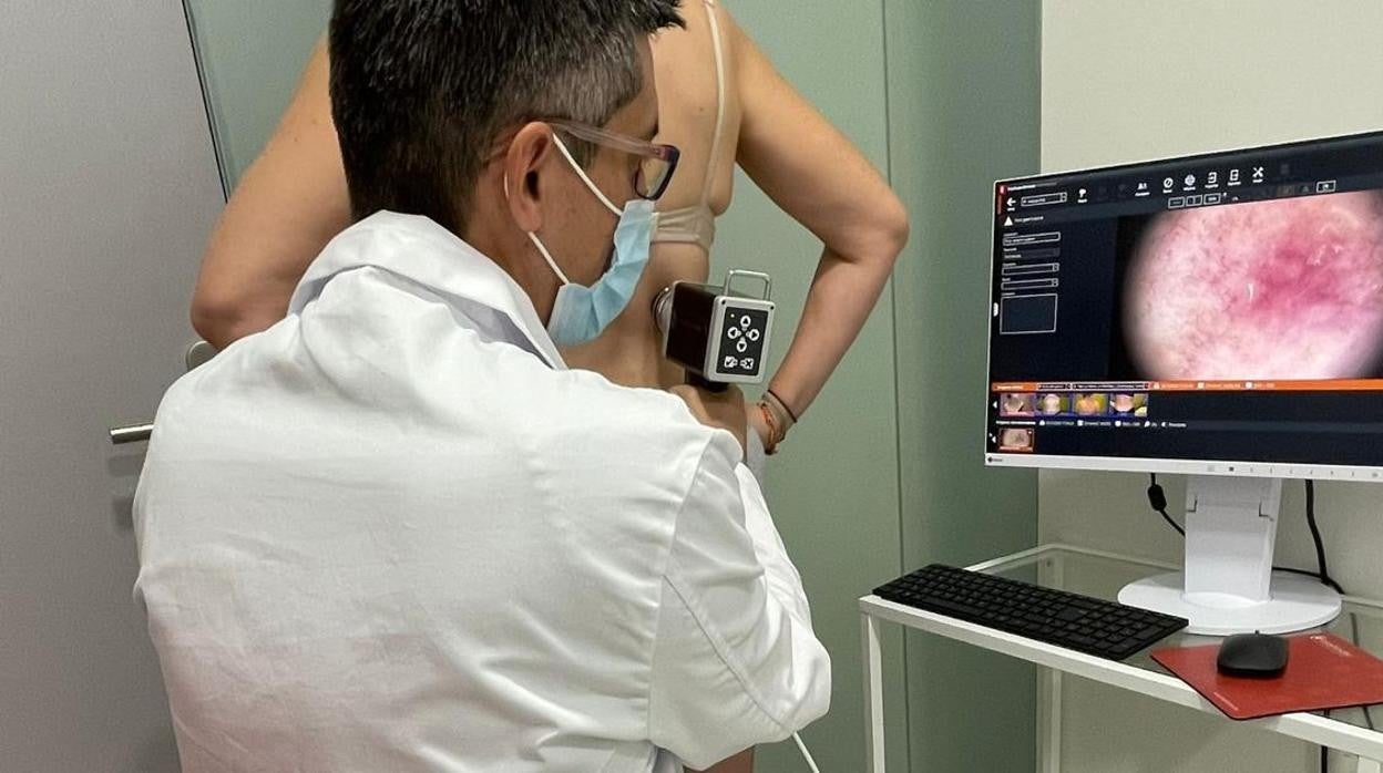 Un facultativo explora la piel a una paciente con un dermatoscopio digital