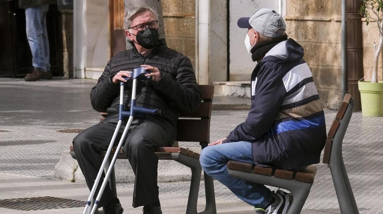 Dos vecinos de Cádiz charlan en la calle con la mascarilla puesta