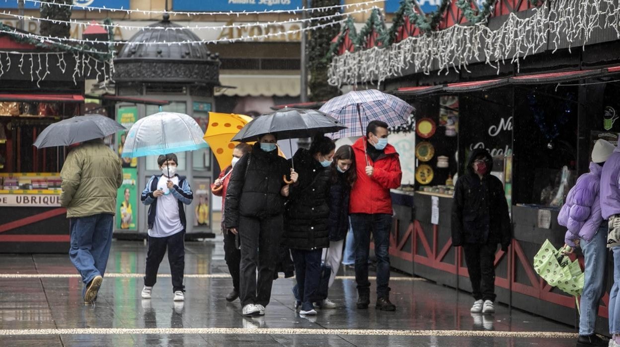 Varias personas visitan con paraguas, en medio de la lluvia, el mercado navideño de las Tendillas