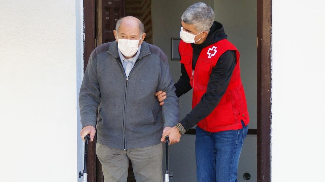 Un trabajador de Cruz Roja ayuda a un señor con andador