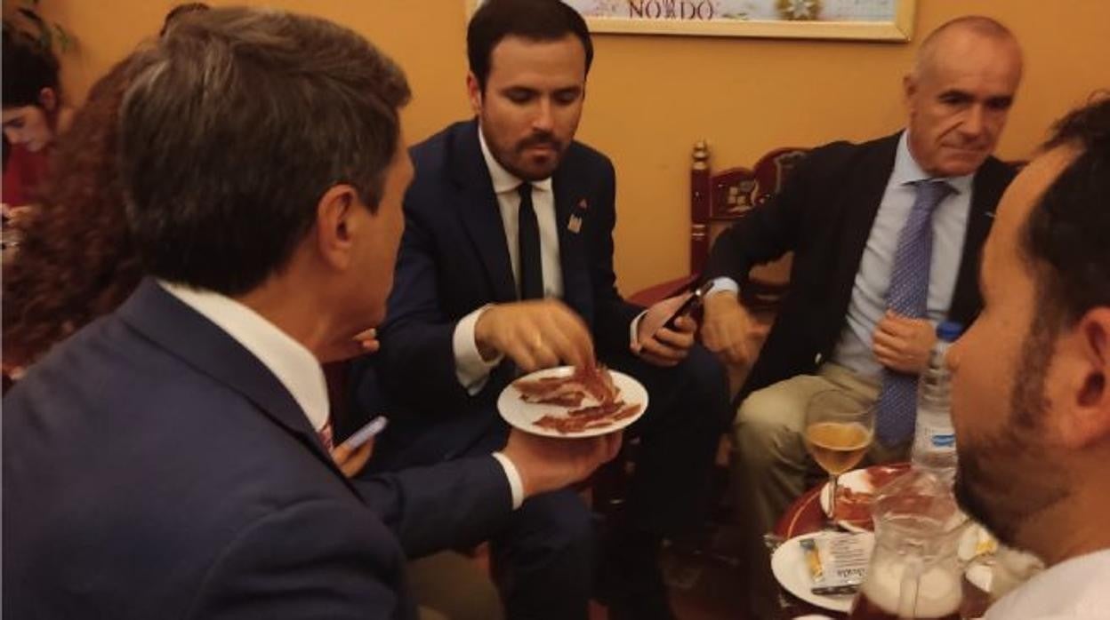 El delegado del Gobierno en Andalucía, de espaldas, Pedro Fernández, le ofrece un plato de jamón al ministro en presencia del alcalde de Sevilla, Antonio Muñoz