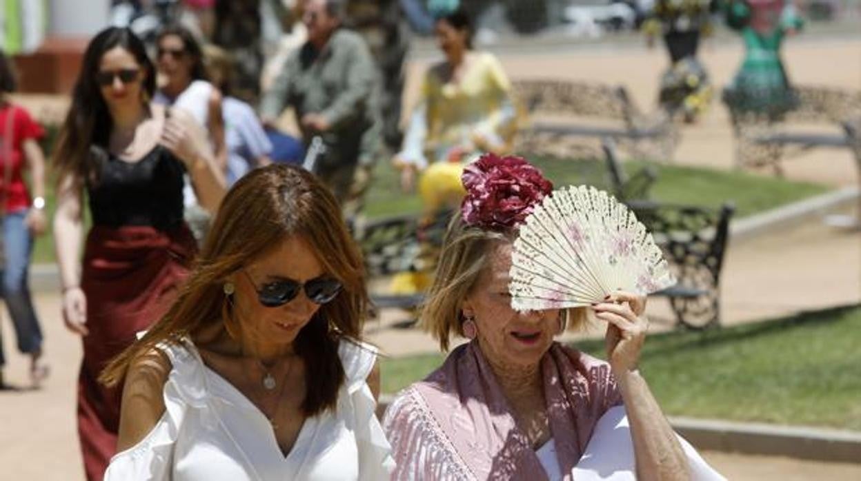 Dos mujeres pasean por la feria tapándose el sol con un abanico