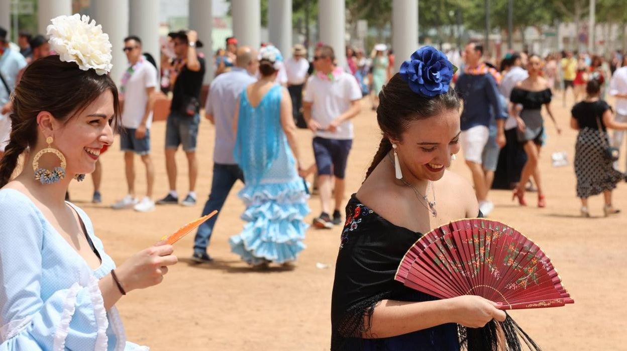 Dos jóvenes vestidas de flamencas se abanican junto a la portada de la Feria de Córdoba