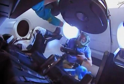 Los miembros de la tripulación de la ISS ingresan en la Crew Dragon de SpaceX por primera vez. Llevan equipos de protección para evitar la respiración de partículas que pueden soltarse durante el lanzamiento