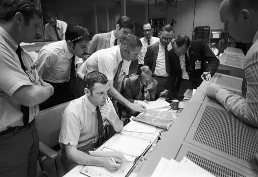 Controladores de vuelo en en la sala de operaciones estudiando un mapa meteorológico del sitio de amerizaje para la misión Apolo XIII