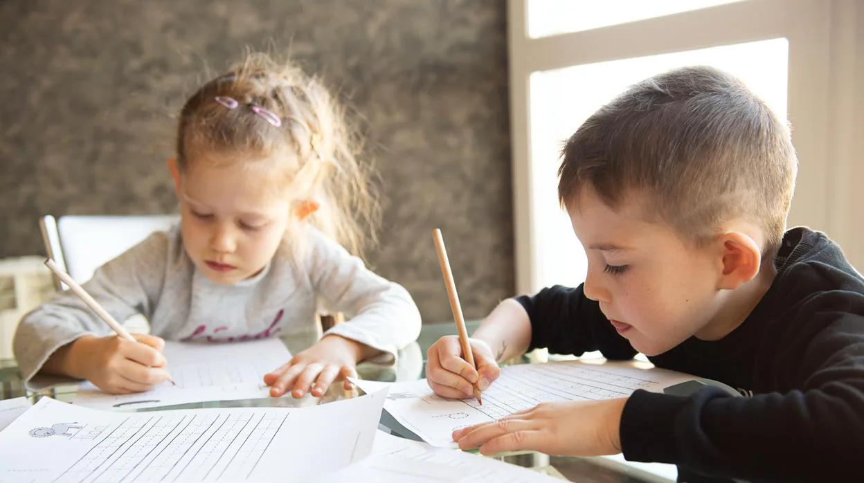 Dos niños escriben con lápiz y papel