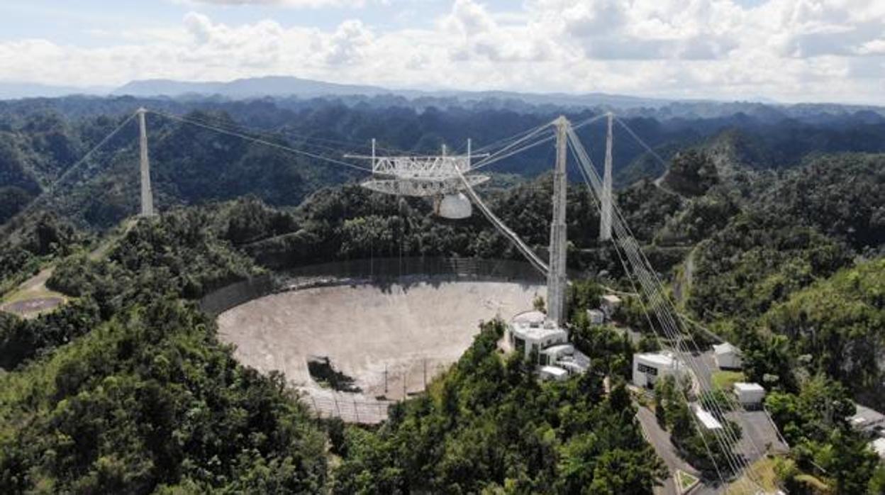 Imagen del radiotelescopio de Arecibo, en Puerto Rico, antes de su derrumbe. Se pueden observar una avería en el plato, a la izquierda, causada por el desprendimiento de un cable