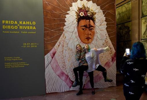 Dos jóvenes se fotografían ante el cartel de la exposición de Frida Kahlo y Diego Rivera