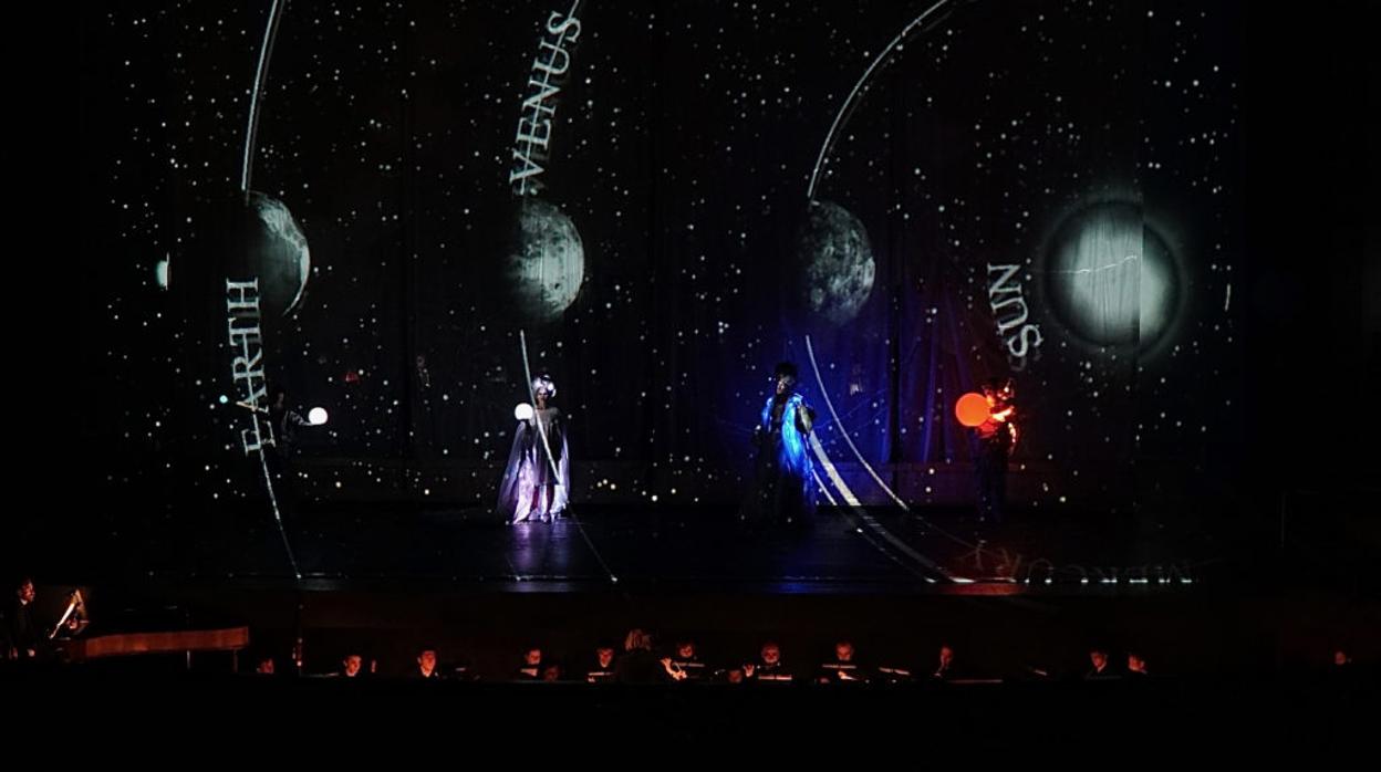 Una escena de la ópera donde incluyen figuras de planetas