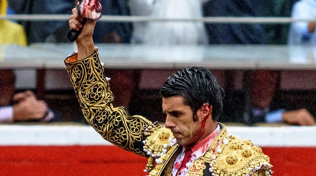 Emilio de Justo, con la oreja izquierda desgarrada y la sangre cayendo por el rostro, muestra la oreja del tercer toro cogida