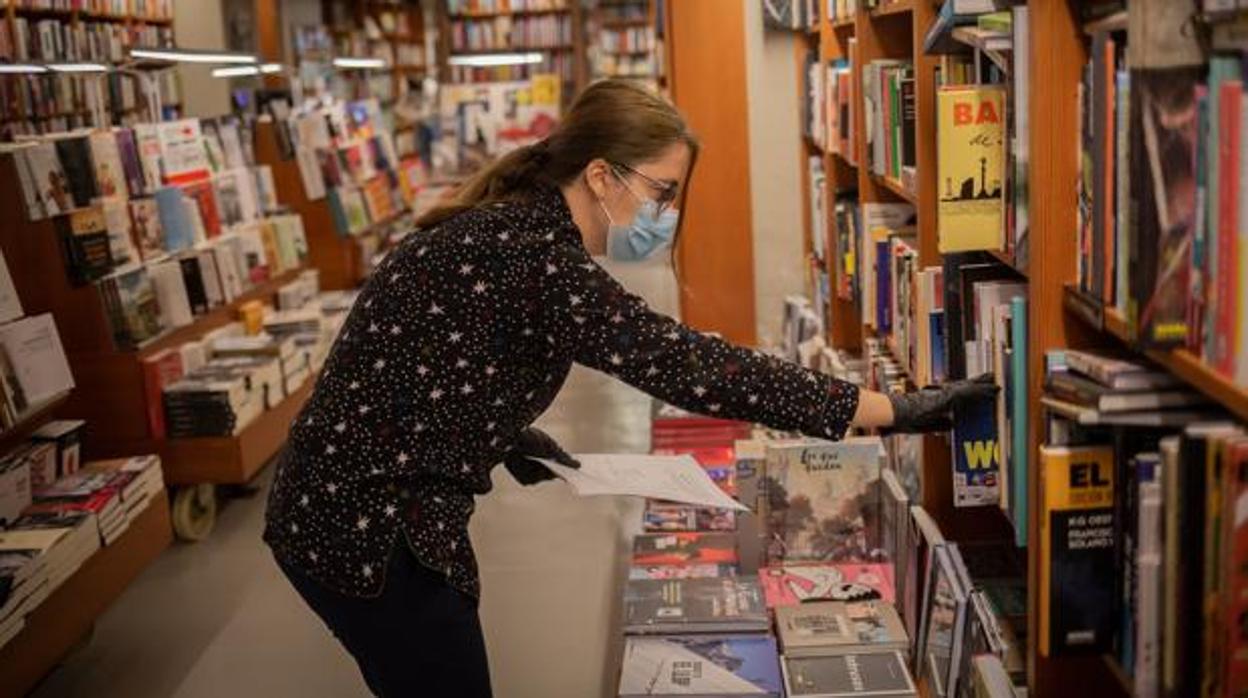 Una trabajadora de la librería Laie Pau Claris de Barcelona coloca libros y material en las estanterías del local