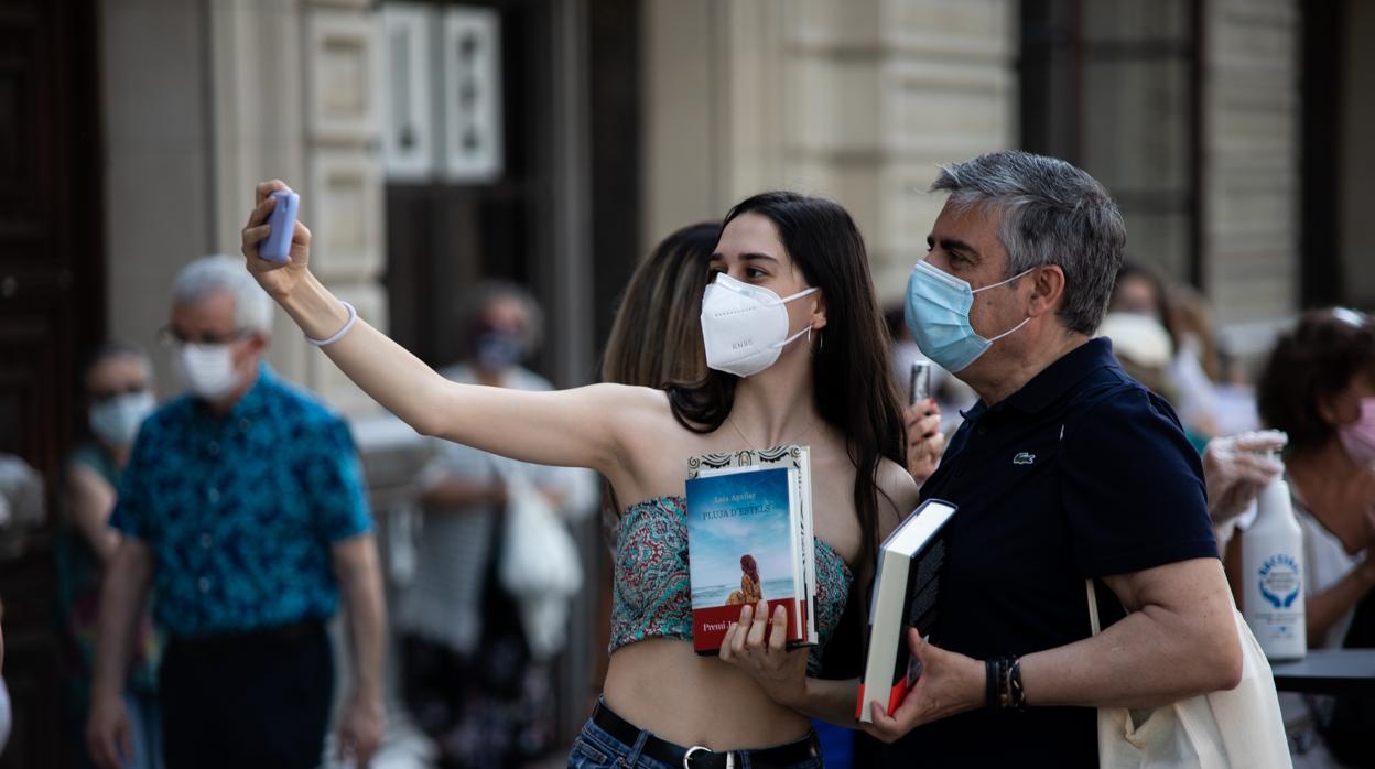 Dos personas se hacen una fotografía cerca de donde han colocado un puesto de libros, en Barcelona