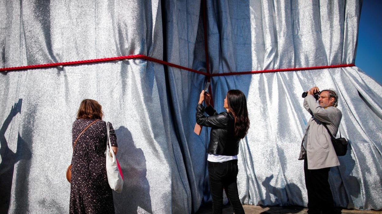 Varias personas hacen fotos al monumento del Arco del Triunfo completamente envuelto por Christo