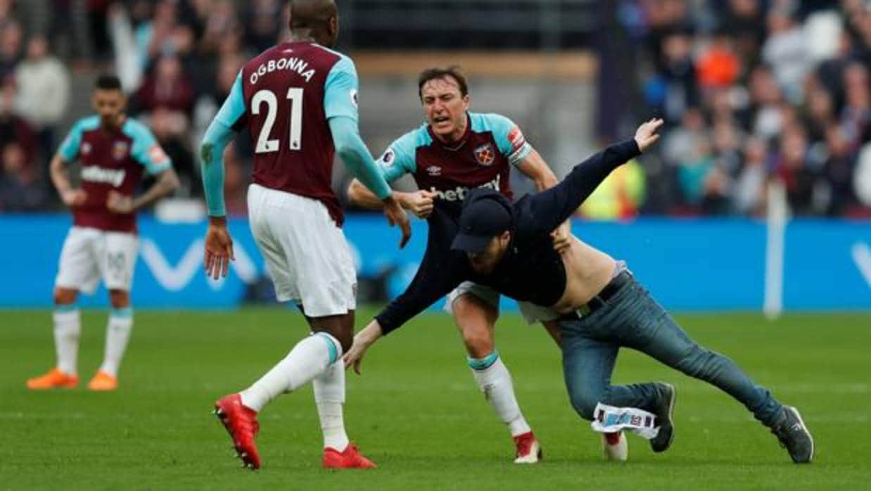 Mark Noble, jugador del West Ham, se enfrenta a uno de los aficionados que han saltado al césped