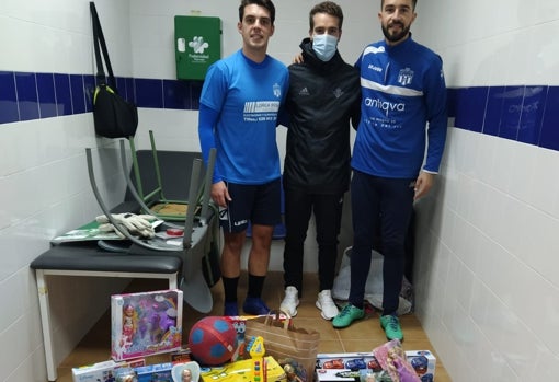 Javier López posa junto a Javi, capitán del Alcalá del Río a su derecha, y con Chico, portero del equipo, a su izquierda, con parte de los juguetesrecaudados