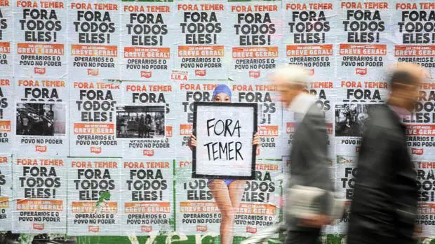 Una persona pasa frente a un muro lleno de carteles en contra del presidente de Brasil, Michel Temer
