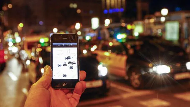 Un cliente pide un coche en Uber mientras taxis y vehículos con conductor por Barcelona
