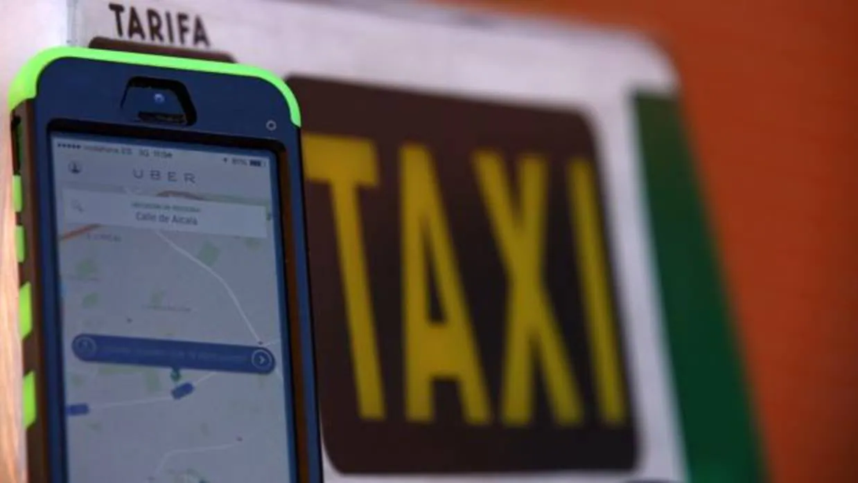 Un teléfono con la aplicación de Uber frente a un taxi