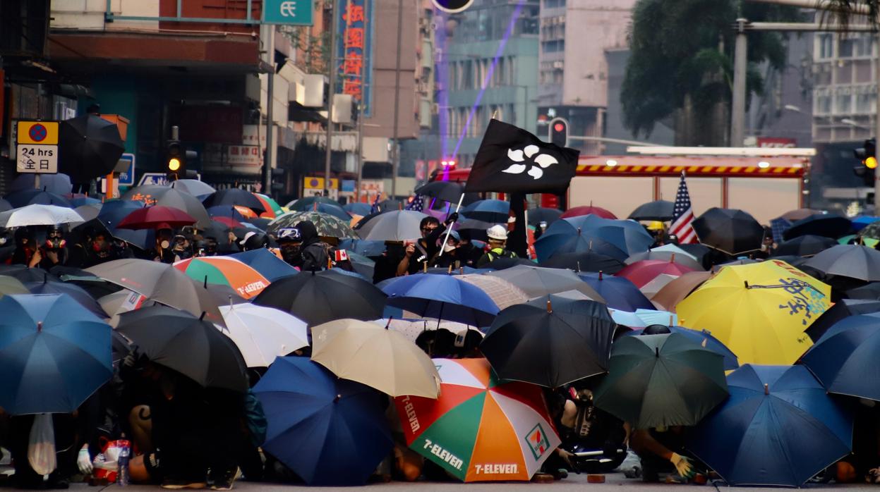 Parapetados tras sus paraguas al modo de la «tortuga romana», los manifestantes ondean una bandera negra de Hong Kong