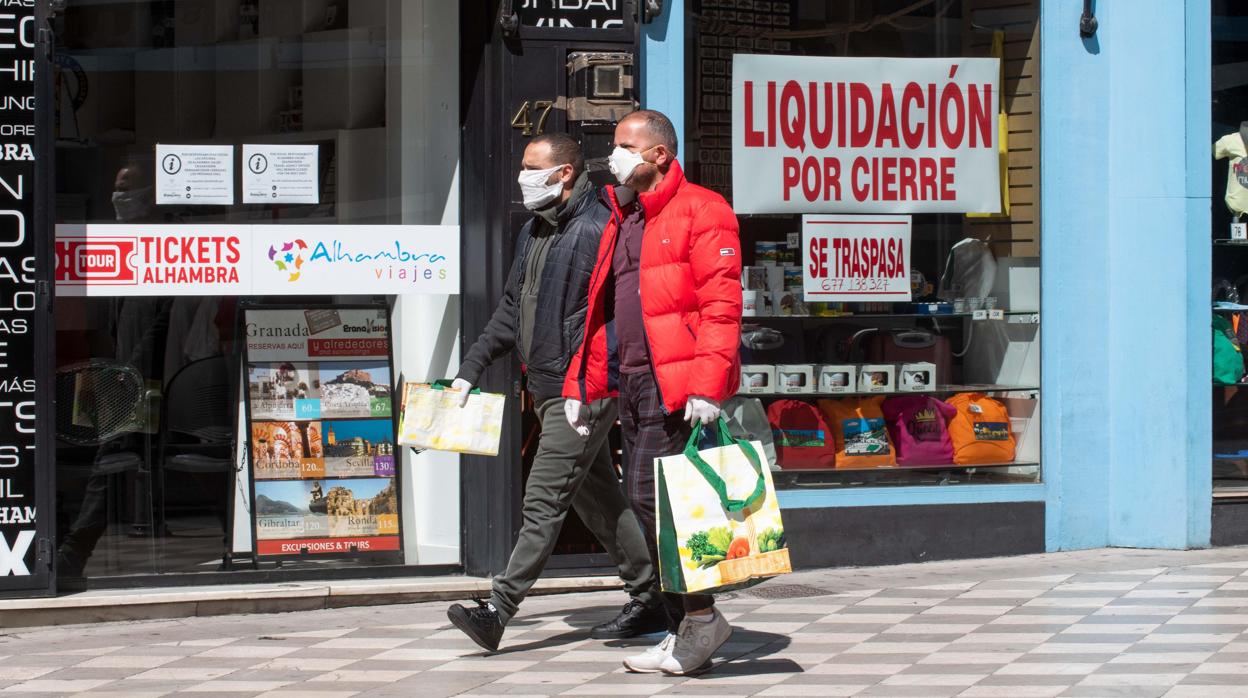 Dos personas protegidas con mascarillas caminan junto a comercios cerrados en Granada