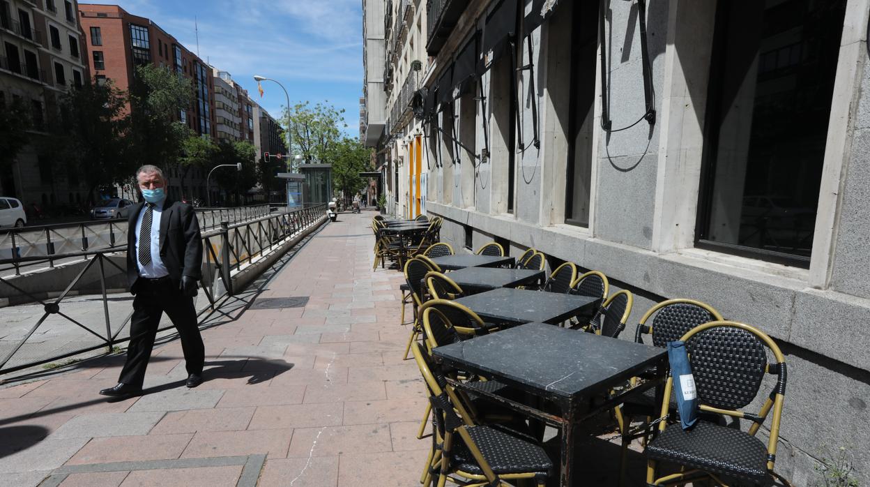 Un hombre con mascarilla pasa junto a una terraza cerrada de un bar en Madrid