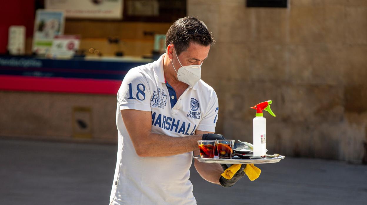 n camarero atiende una mesa equipado con mascarilla y con un espray desinfectante en el centro de Vitoria