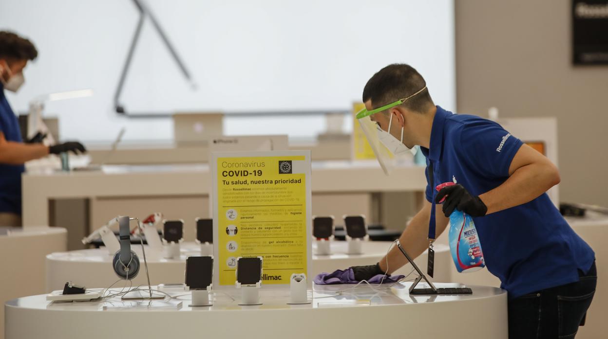 Un trabajador desinfecta un expositor en una tienda de tecnología del centro comercial Lagoh de Sevilla