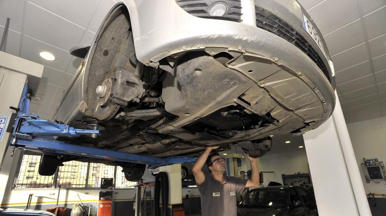 Un trabajador inspecionado los bajos de un coche en un taller de automoción