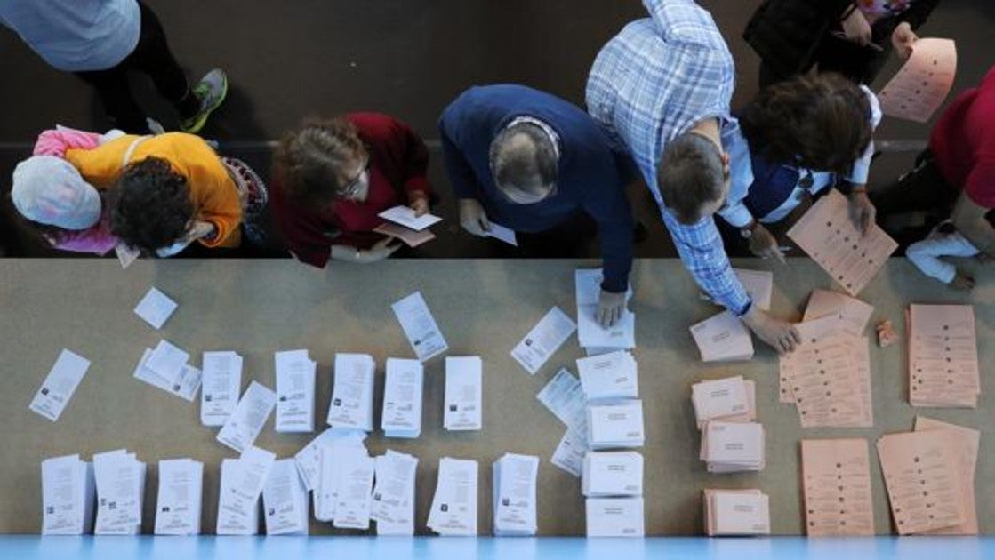 Votantes ante una mesa con papeletas en un colegio electoral