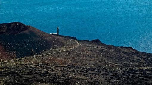 La arena volcánica de El Hierro desemboca en el mar con el faro de Orchilla como testigo