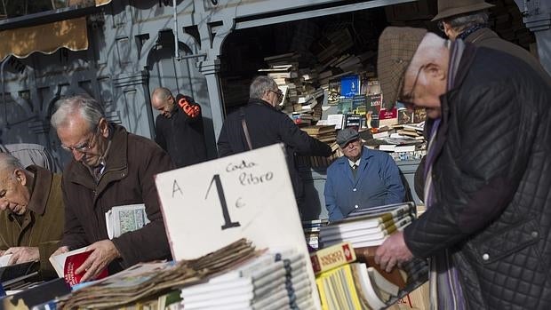 Varios clientes hojean libros en la Cuesta de Moyano, ante la mirada de uno de los libreros