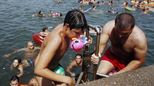 Un niño sale del agua con un pato de goma en la boca.