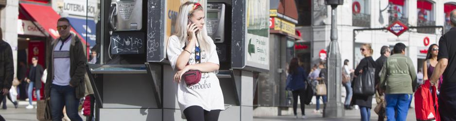 Una joven habla por el teléfono móvil, apoyada en una cabina de la Puerta del Sol