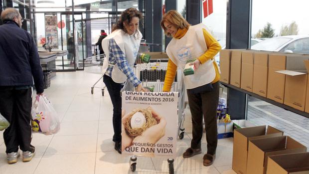 Dos voluntarias colocan alimentos en un carro de la compra
