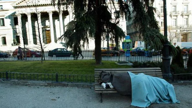Una persona sin hogar duerme en un banco frente al Congreso de los Diputados