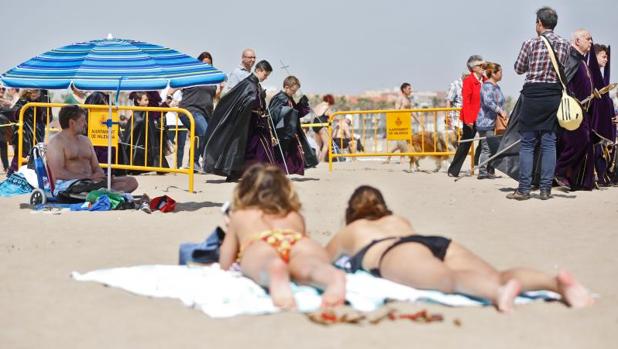 Gente tomando el sol mientras pasa una procesión marinera en la playa de València