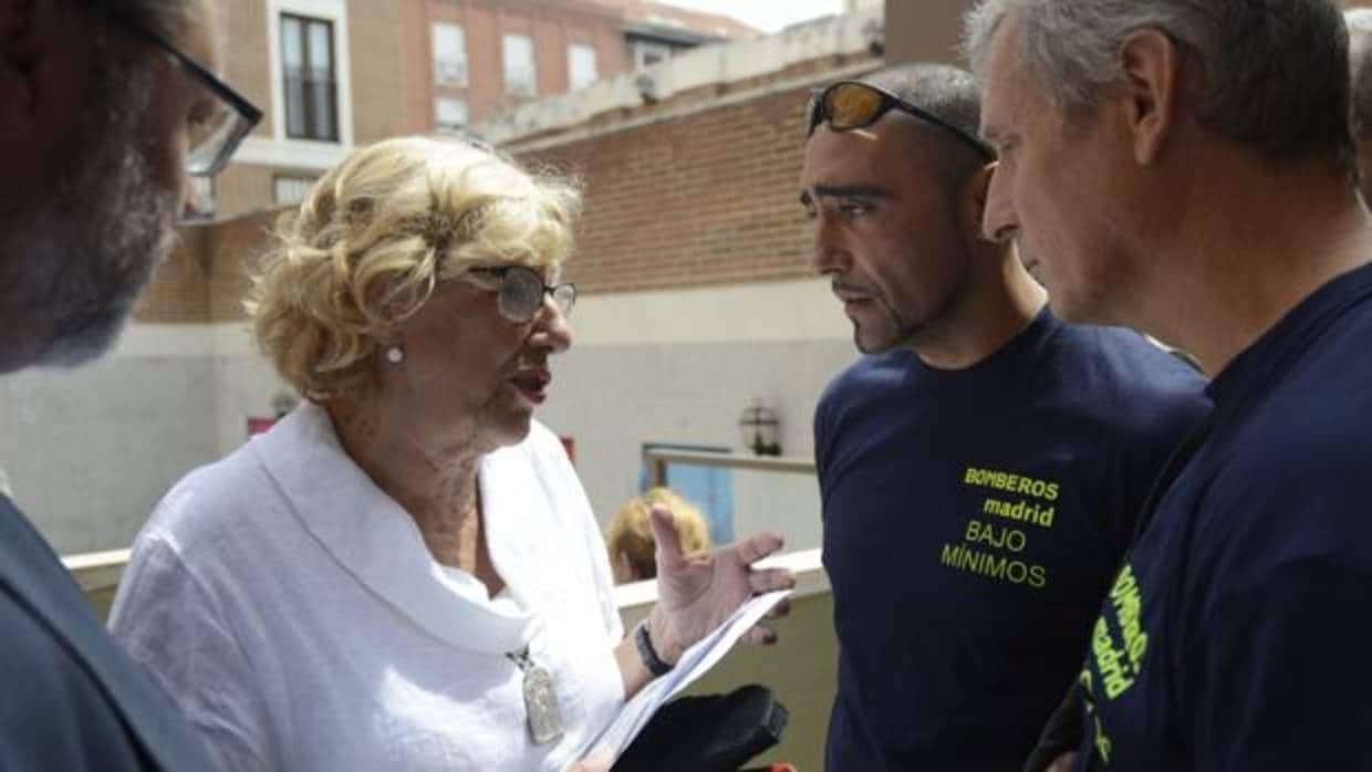 Manuela Carmena habla con algunos bomberos, en la fiesta de La Paloma