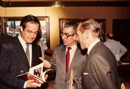 José Bono repasa el Catálogo de la exposición «Que la llama del arte siga viva», mientras charlan con él Sánchez-Colorado y Tomás Camarero