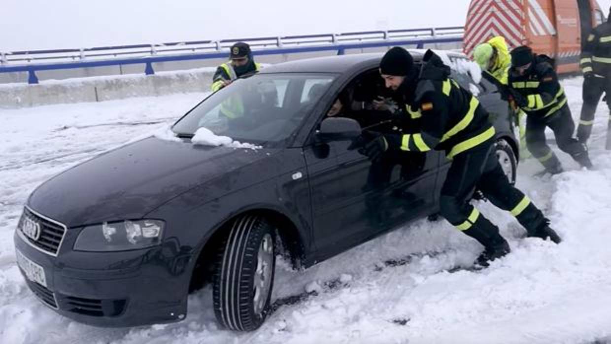 Un equipo de rescate de la UME, junto a un guardia civil, tratan de rescatar un coche atrapado en la nieve