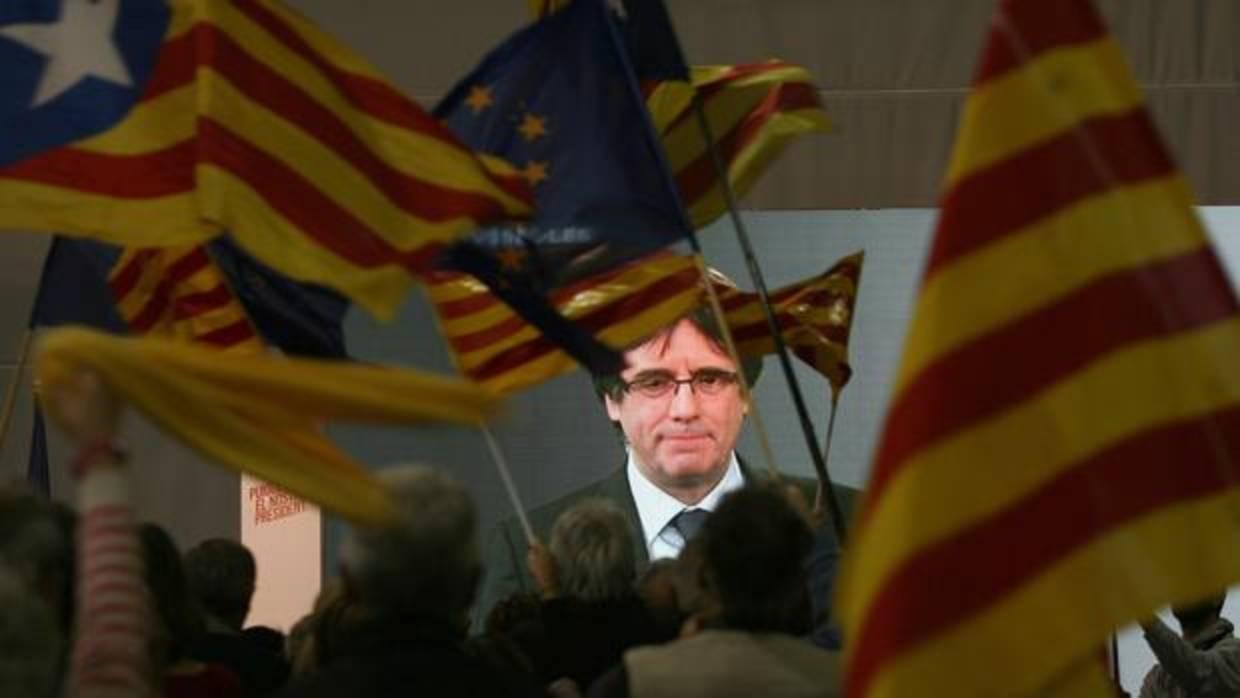 Rostro del prófugo Puigdemont proyectado en una pantalla ante espectadores con banderas independentistas